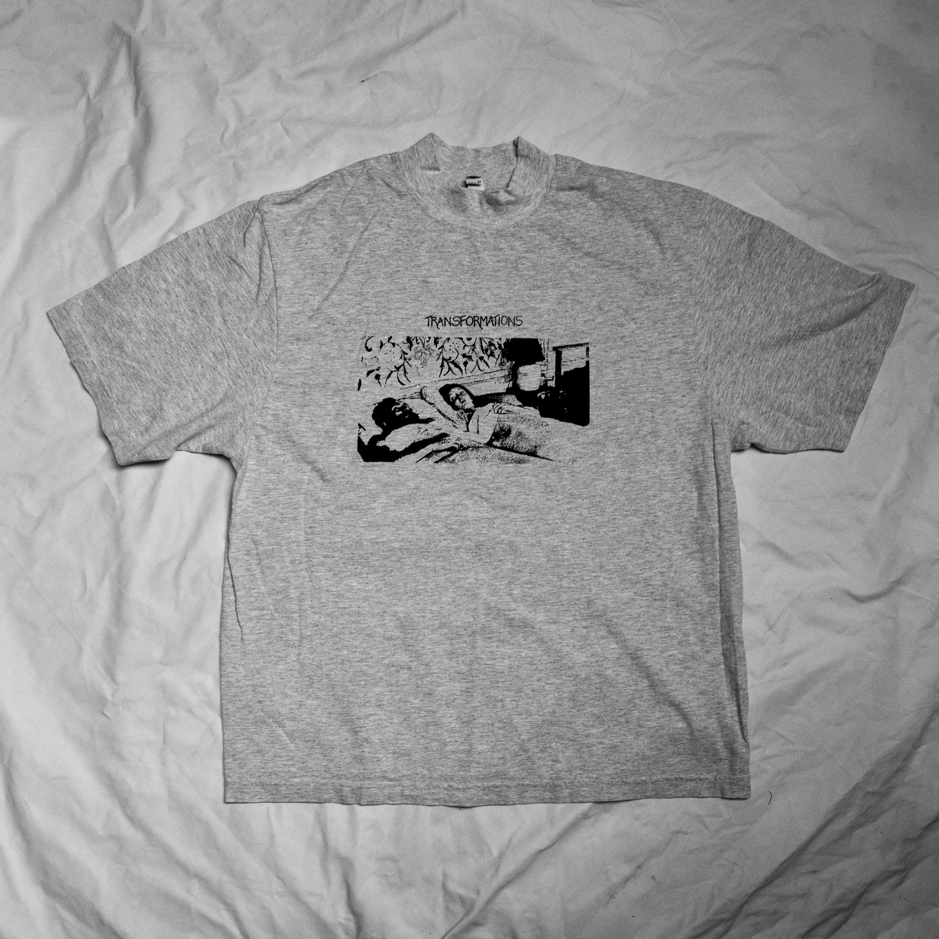 A gray t-shirt with a mockneck design featuring a black and white film still of a group of people, from a scene from the short film 'Transformations'.